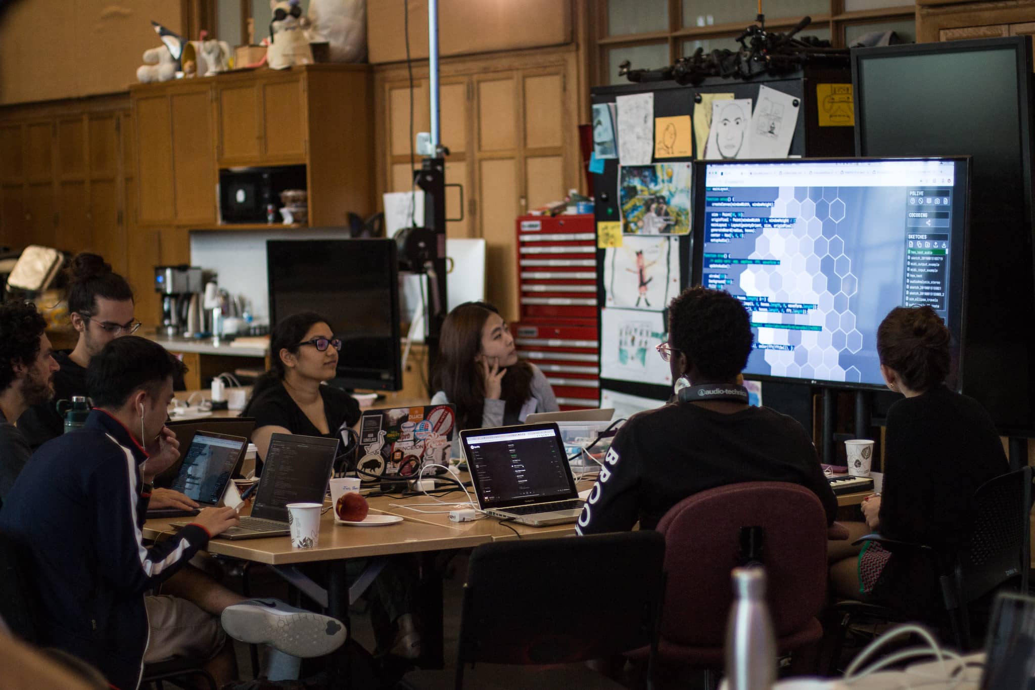 Participants sit around a table with their laptops and observe code on a screen"